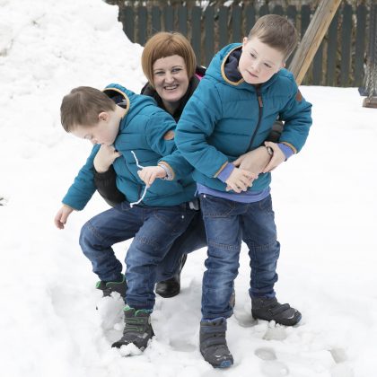 Na snegu se ženska igra z dvema otrokoma.
